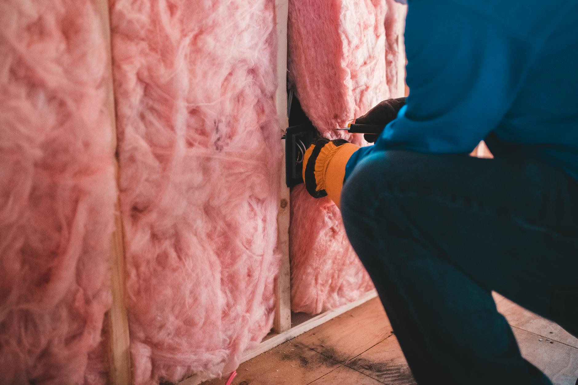 Styropian, wełna, pianka PUR – porównanie kosztów docieplenia domu Pracownik ocieplający dom różową wełną mineralną